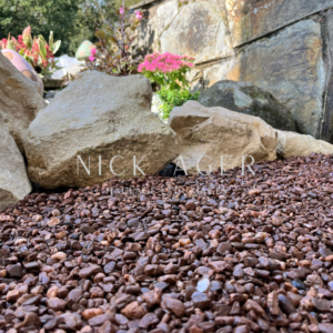 A close-up view of brown gravel and large stones in a landscaped garden with colourful plants in the background.