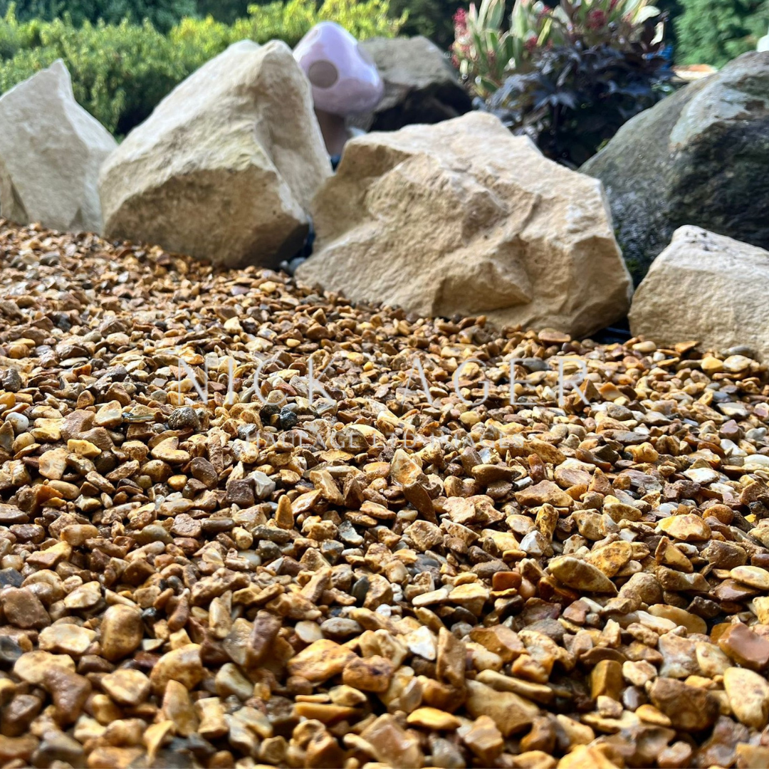 A close-up view of finely crushed gravel with a mix of brown and tan hues, surrounded by large, smooth rocks in a landscaped garden.