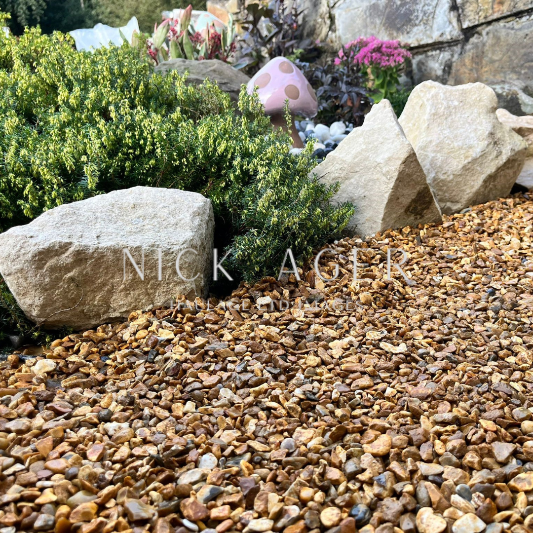 A vibrant garden scene featuring colourful gravel, large rocks, and lush greenery, with a decorative pink mushroom in the background.