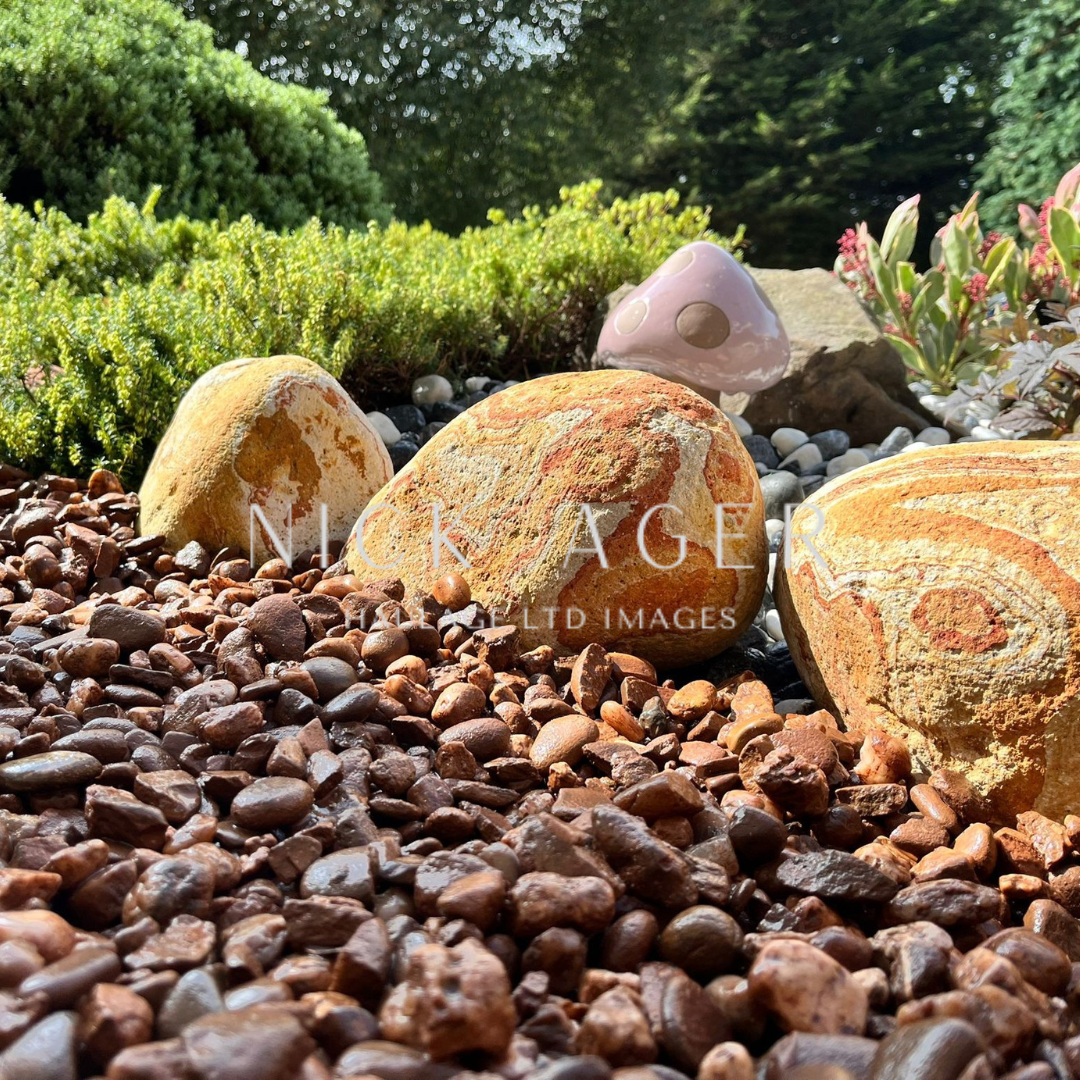 A close-up view of decorative garden stones with vibrant patterns, surrounded by brown gravel and green foliage.