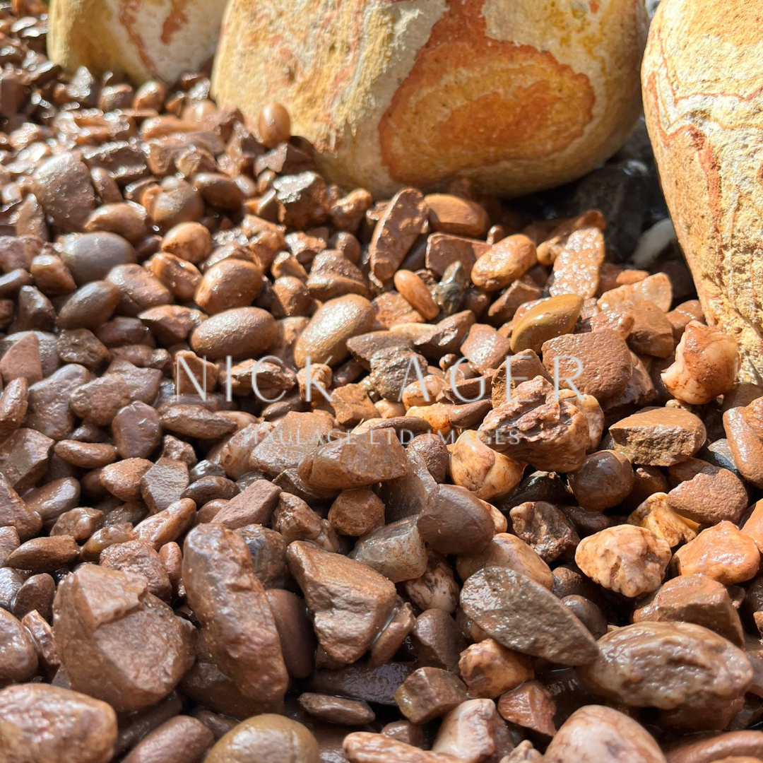 A close-up view of a mixture of brown pebbles and stones, with water droplets visible on the surface, featuring larger stones in the background.
