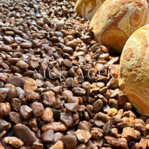 A close-up view of small brown pebbles scattered on a surface, with larger stones partially visible in the background, reflecting light.