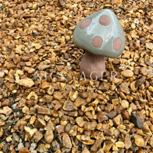 A decorative ceramic mushroom with a green cap and brown spots, standing on a bed of small, pebbly gravel stones.