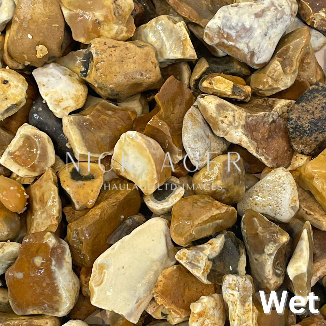 A close-up view of assorted wet pebbles and stones in various shapes and colours, including orange, brown, and cream, glistening with water.