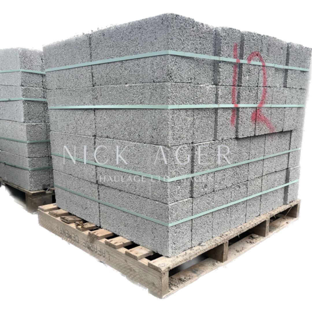 Close-up view of stacked grey concrete blocks secured with green straps on a wooden pallet, with a number 12 marked in red on one block.