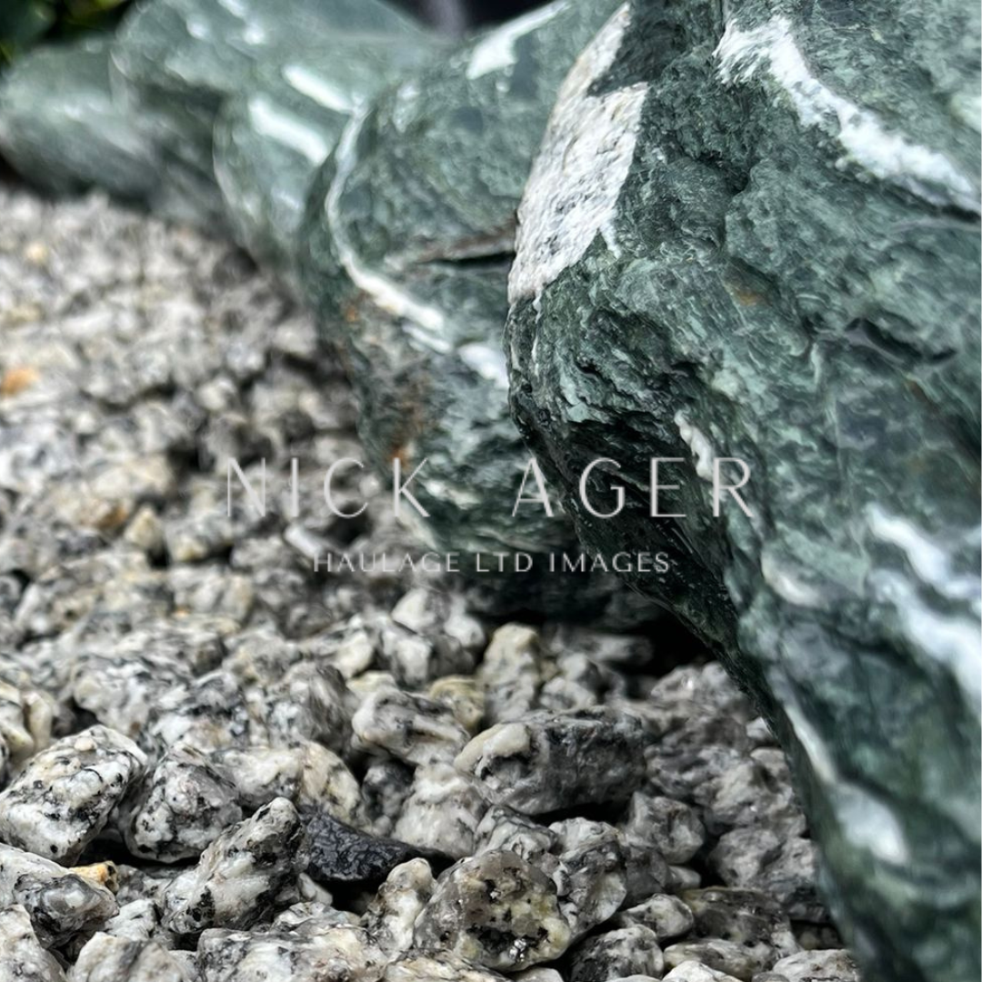 A close-up view of a green rock resting on a bed of grey gravel, showcasing the texture and colour variations of both surfaces.