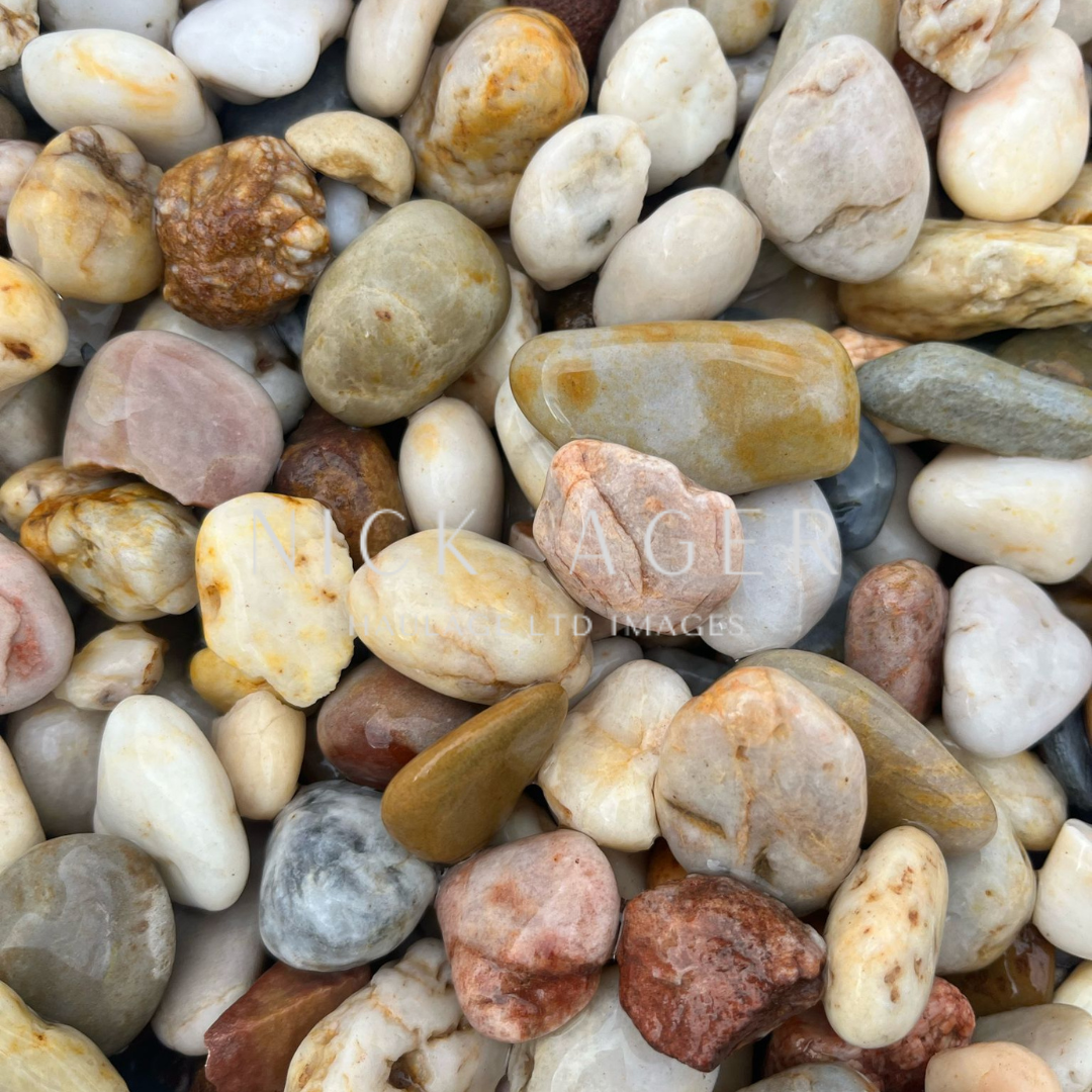 A close-up view of various smooth pebbles and stones in a mix of colours including tan, grey, white, and brown, forming a textured surface.