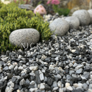 A close-up view of a garden area featuring a mix of black and white gravel stones, surrounded by lush greenery and large decorative rocks.