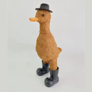 A whimsical decorative duck sculpture made from straw-like material, wearing a black hat and rubber boots, standing against a plain background.
