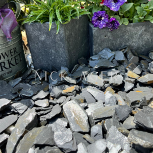 A close-up view of a garden bed featuring dark slate stones, two rectangular planters with green plants, and purple flowers.