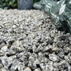 A close-up view of small, grey and white decorative stone gravel scattered on the ground, with larger green stones visible in the background.