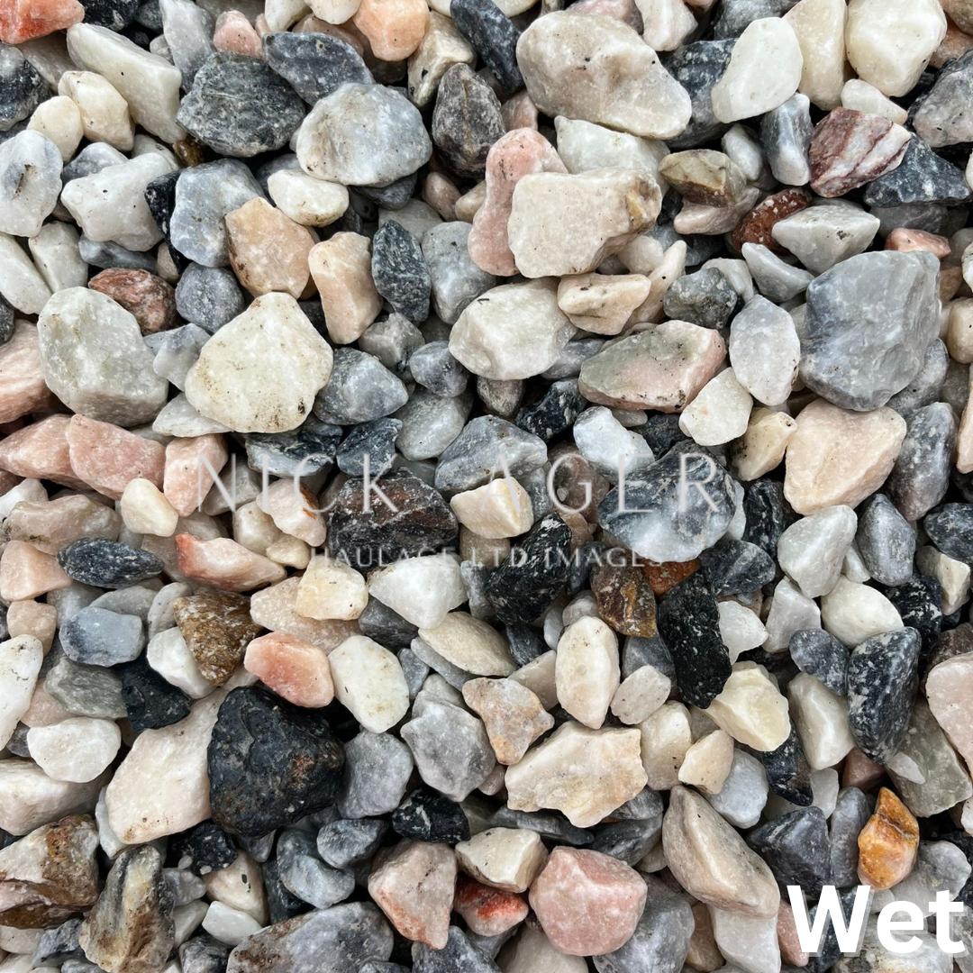 A close-up view of wet mixed gravel stones in various shapes and colours including pink, grey, and black.