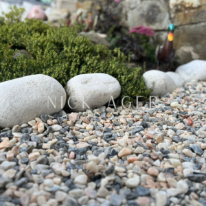 A close-up view of decorative stones and large round rocks in a garden, with lush green foliage in the background.