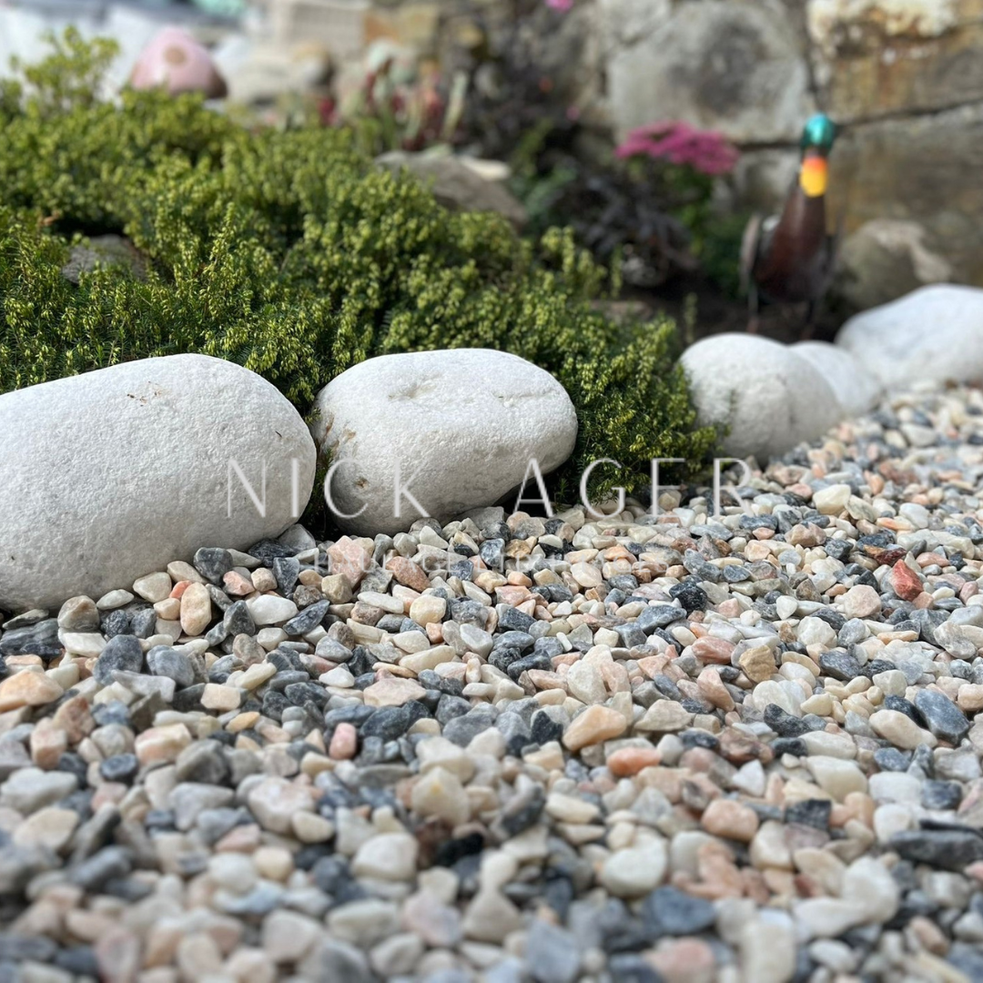 A close-up view of decorative stones and large round rocks in a garden, with lush green foliage in the background.