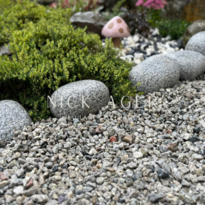 A serene garden scene featuring smooth grey stones bordered by green plants and small pebbles, with a pink mushroom decoration peeking through the foliage.