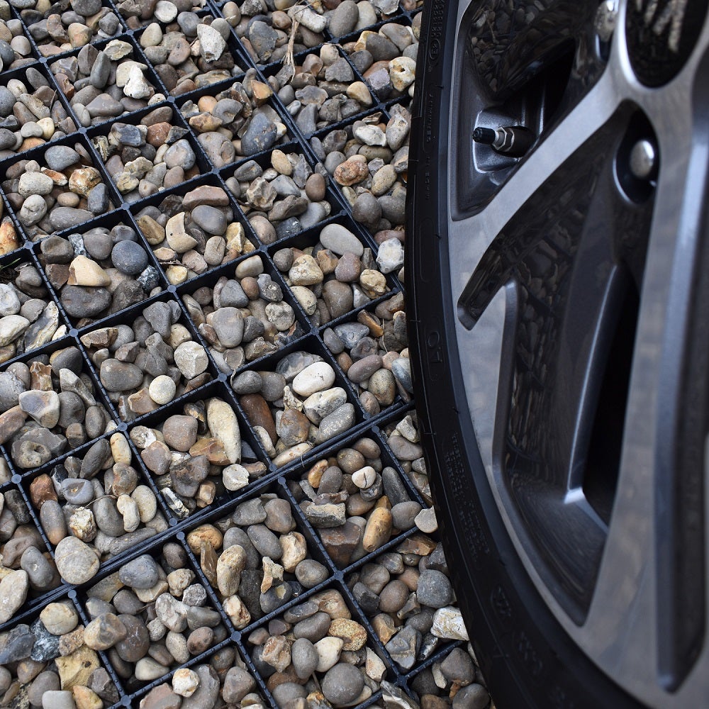 A close-up view of a gravel driveway featuring small stones held in place by a plastic grid, with a car tyre partially visible at the edge.