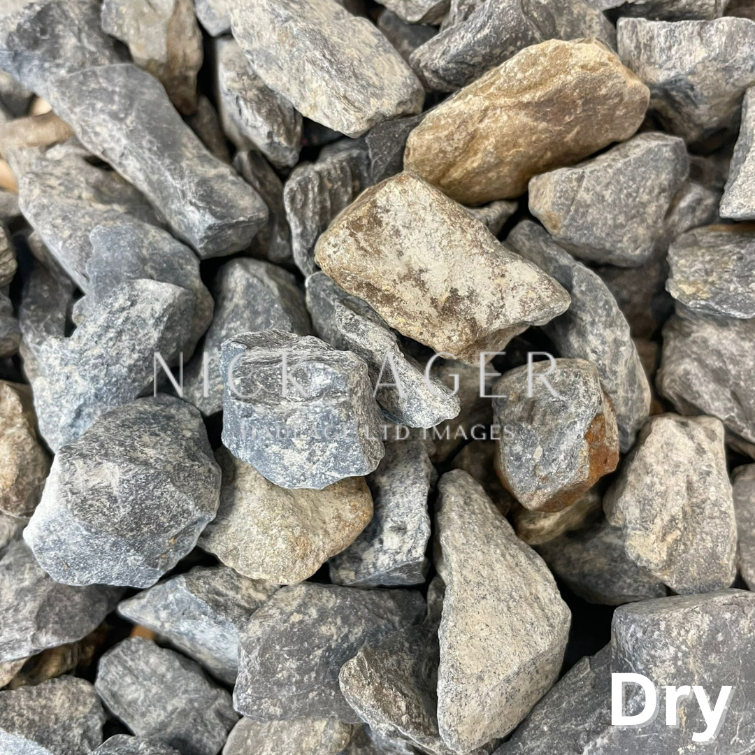 A close-up view of assorted dry gravel stones featuring shades of grey and brown, varying in size and shape.