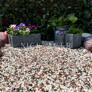 A vibrant garden scene featuring colourful flowers in a grey planter, a decorative tin marked 'Flower Market', and a variety of decorative stones on the ground.