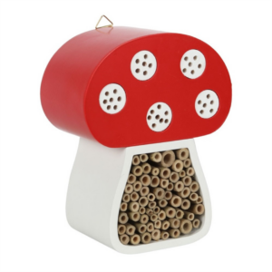 A whimsical mushroom-shaped insect hotel featuring a red cap with white dots and a beige body filled with hollow tubes for insects.