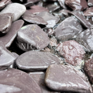 A close-up view of smooth, rounded purple stones partially submerged in clear water, with reflections and textures visible.