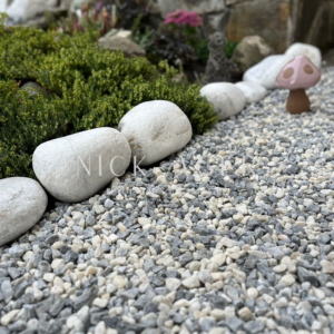 A garden pathway featuring white smooth stones lining the edge, grey and white gravel below, and a small mushroom sculpture amidst greenery.