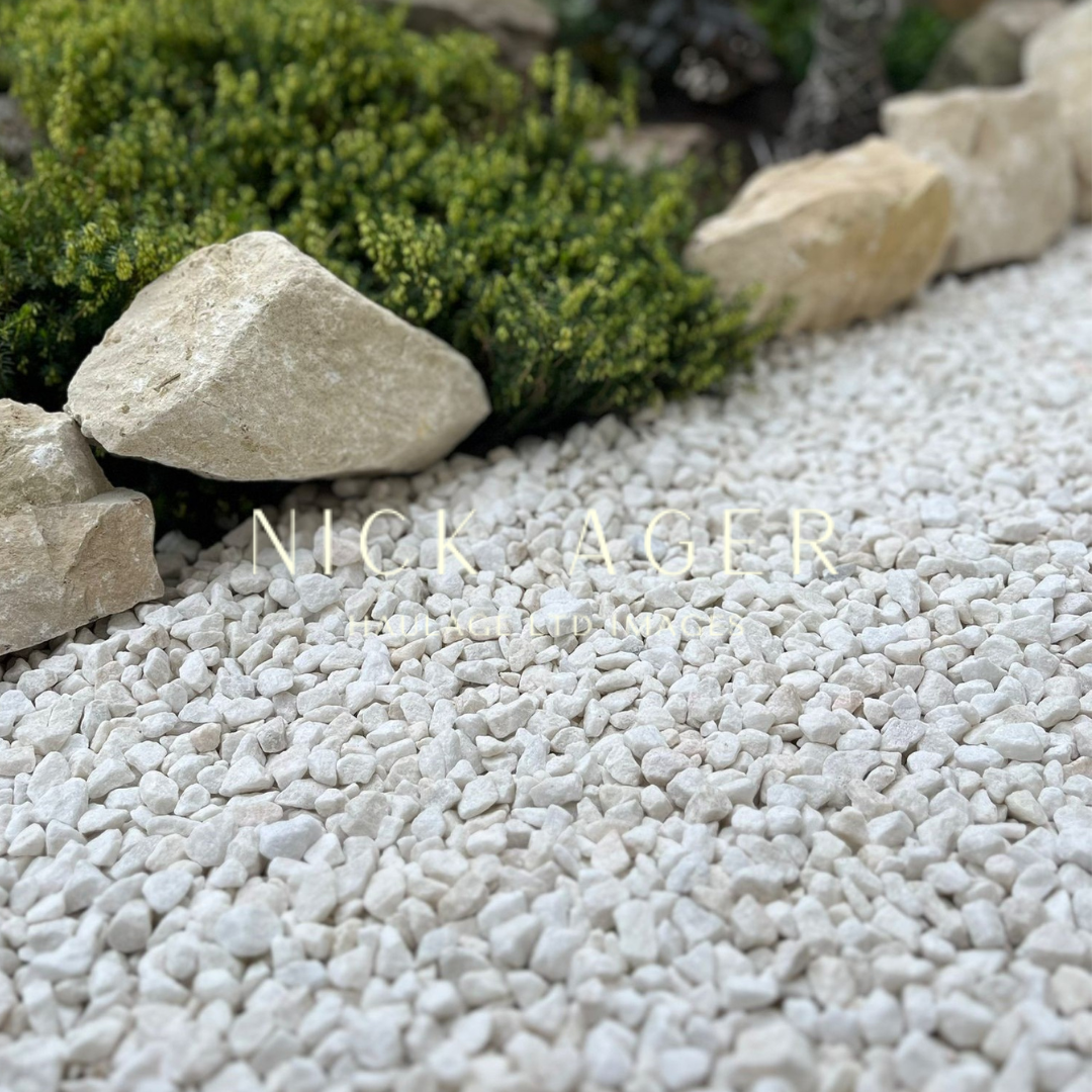 A close-up view of white gravel stones with larger rocks and greenery in the background, showcasing a landscaped garden area.