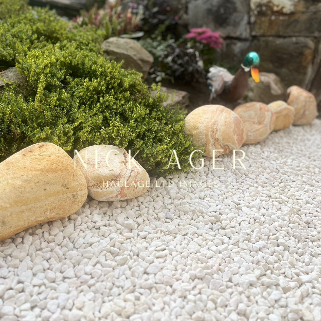A garden scene featuring a variety of decorative stones, a lush green bush, and a decorative duck figure among gravel