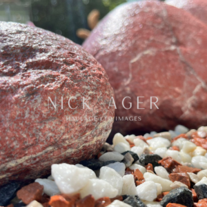A close-up view of two large red decorative stones on a bed of small, multi-coloured pebbles, including white, black, and reddish tones, with a soft focus background.