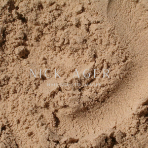 A detailed view of fine sand with a soft texture, displaying various grains and shades of beige, with superimposed text.