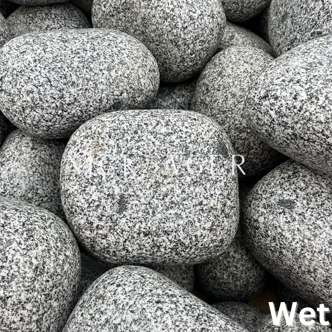 A close-up image of smooth, grey stones with a wet appearance, stacked closely together.