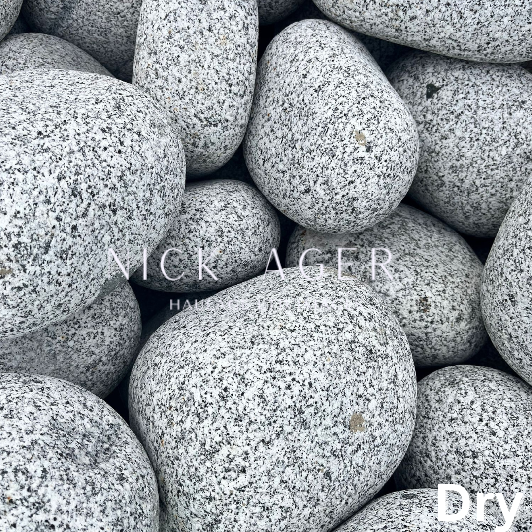 A close-up view of smooth grey decorative stones, showcasing their rounded shapes and speckled texture, arranged closely together.