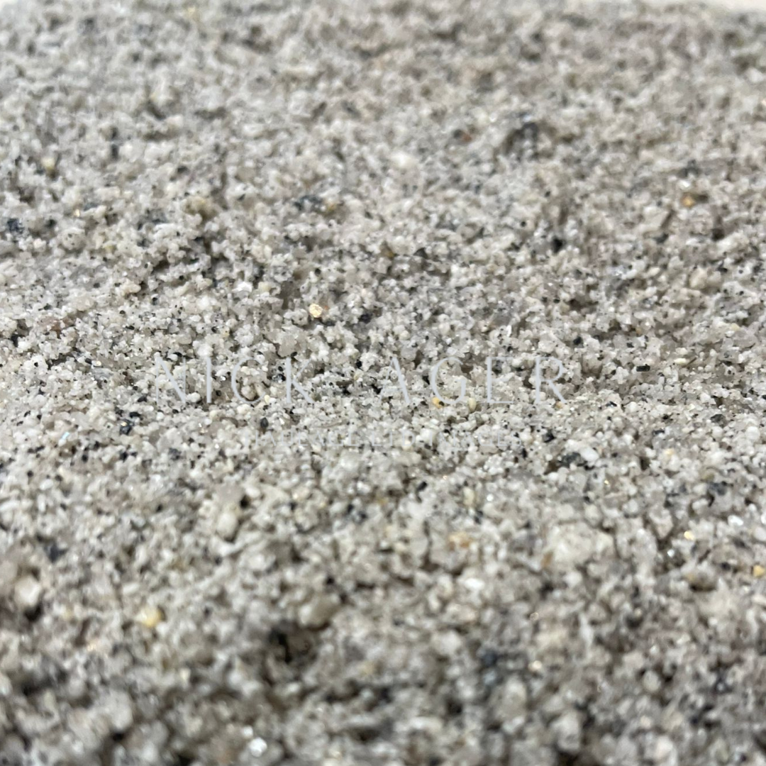 A close-up view of fine grey sand, showcasing a mix of small grains with a slightly reflective surface and varied hues.