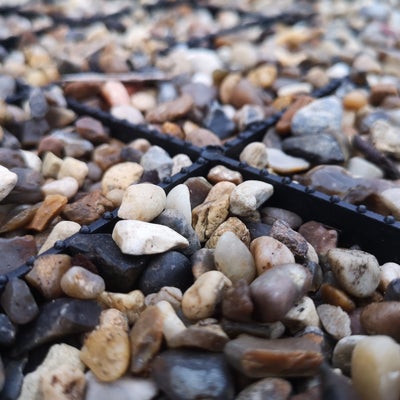 A close-up image of small pebbles and gravel with a black cross design made from plastic or rubber resting on the surface.